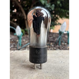 May include: A vintage RCA Radiotron UX 201-A valve. The clear glass bulb reflects the surroundings, with a black base bearing the RCA Radiotron logo and model details. The valve has two metal pins at the base.