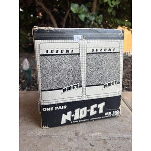 Puede incluir: Una caja de sistema de altavoces Suzuki N-10-CT vintage. La caja es blanca y negra con el logotipo de Suzuki y "N-10-CT" impreso. La caja dice "One Pair" y "2-Way Coaxial Amplified Speaker System".