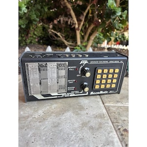 May include: Black MorseMatic MW-2 device with a keypad, knobs, and various labeled sections. The device has a black exterior with yellow keys and white text. The text includes "Advanced Electronic Applications Inc."