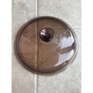 Puede incluir: Una taza de cerámica blanca con un asa negra y el texto "But First, Coffee" en negrita negra. La taza se encuentra sobre un fondo borroso, sugiriendo un ambiente acogedor.