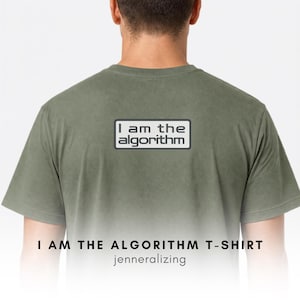 May include: An olive green short-sleeved t-shirt featuring a rectangular graphic on the back. The graphic contains the text "I am the algorithm" in a dark gray sans-serif font, enclosed within a thin dark gray border on a light gray background.
