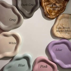Peut inclure: Une collection de petits plateaux de forme irrégulière, de couleurs variées : gris, blanc, gris foncé, bleu, rose et lilas. Certains plateaux ont un effet marbré brun clair et foncé. Chaque plateau est étiqueté avec son nom de couleur.