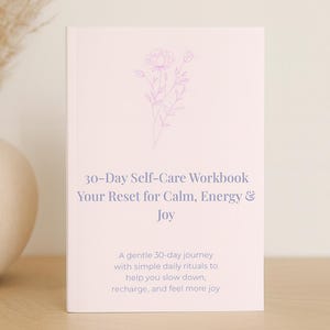 Puede incluir: Un cuaderno de trabajo de autocuidado de 30 días de color rosa pálido con el texto "Your Reset for Calm, Energy & Joy". La portada presenta una delicada ilustración floral. El libro promete un viaje suave de 30 días con rituales diarios.
