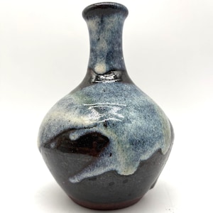 May include: A small, handcrafted ceramic vase with a rounded body and a narrow neck. The vase features a dark brown base, transitioning to a blue and white glaze. The top rim is a darker shade of brown.