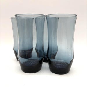 May include: Four blue-tinted drinking glasses. The glasses have a dark blue base that fades to a lighter blue towards the top. The glasses are cylindrical with a slightly flared top.