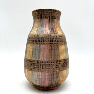 May include: A ceramic vase with a rounded body and a narrow neck, featuring a vertical striped pattern in shades of pink, blue, and brown, accented by two horizontal bands of a dark, textured, grid-like design in a metallic gold finish.