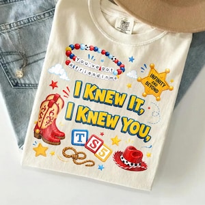May include: A cream-colored t-shirt featuring a graphic print with a red cowboy boot, a red cowboy hat, a beaded bracelet with the text 'You've got a friend in me', a sheriff badge with 'INFINITY AND BEYOND', and the text 'I KNEW IT, I KNEW YOU, TS5'.