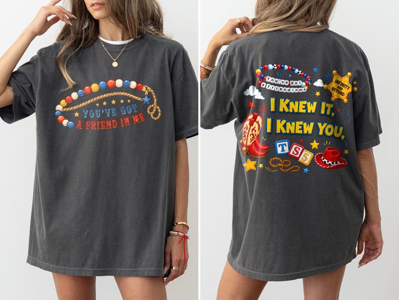 Pu&ograve; includere: Una t-shirt grigio antracite a maniche corte con una grafica frontale di una collana di perline colorate e il testo "YOU'VE GOT A FRIEND IN ME". Il retro mostra una grafica pi&ugrave; grande con stivali da cowboy, un cappello, blocchi e il testo "I KNEW IT, I KNEW YOU".