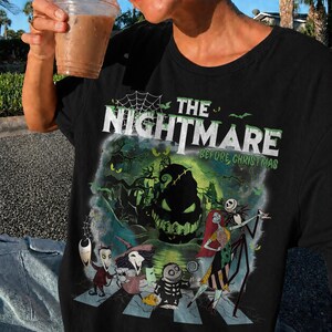 May include: Black t-shirt featuring a graphic from "The Nightmare Before Christmas." The design includes characters like Jack Skellington and Sally crossing a street, with the film's title in green and white.