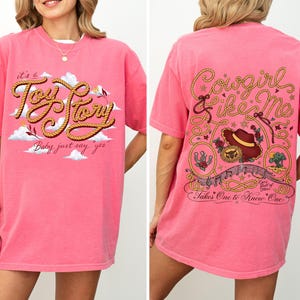 May include: A bright pink short-sleeve t-shirt featuring a front graphic with the text 'it's a Toy Story Baby, just say yes' and a back graphic with the text 'Cowgirl like Me' and 'Takes One to Know One' surrounded by rope, hat, and floral motifs.
