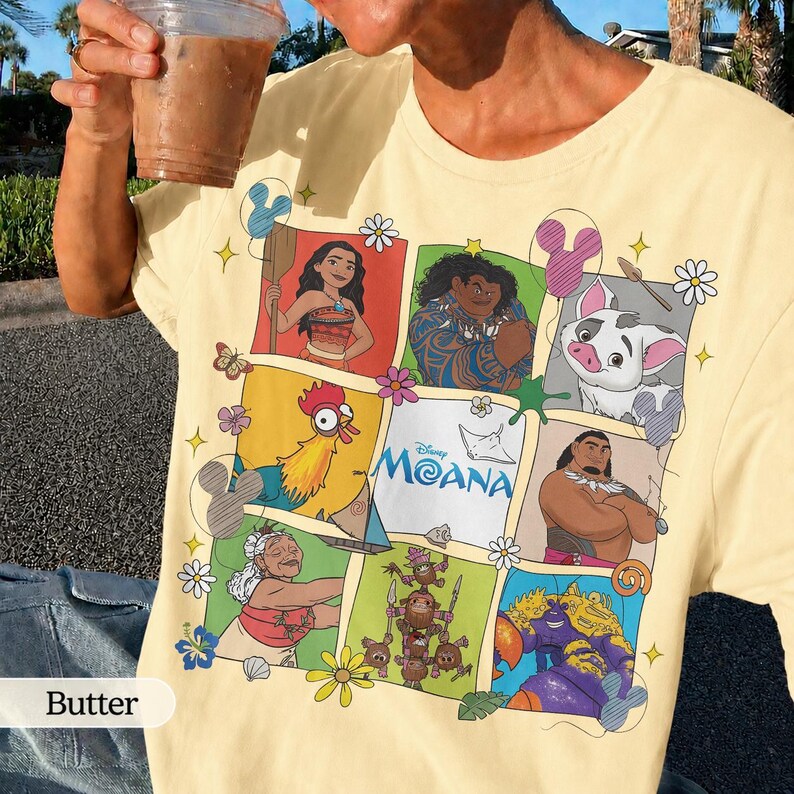 Op de afbeelding: Boterkleurig T-shirt met een rasterontwerp van Moana-personages. Het ontwerp bevat illustraties van Moana, Maui, Pua, Hei Hei en anderen, met het Disney Moana-logo. Het shirt heeft een klassieke ronde hals en korte mouwen.