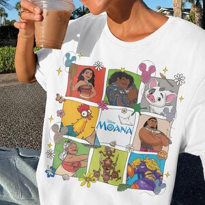 Op de afbeelding: Wit T-shirt met een kleurrijke afbeelding van personages uit de Disney-film Moana. Het ontwerp bevat afbeeldingen van Moana, Maui, Pua, Hei Hei en anderen, met het logo van de film. Het is een casual kledingstuk.