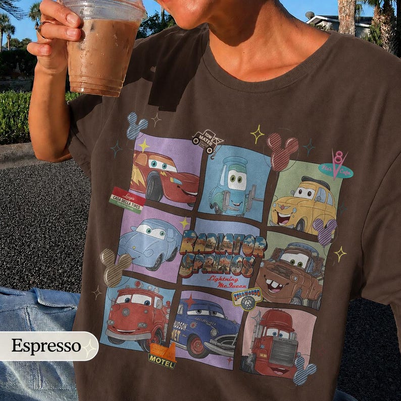May include: A dark brown t-shirt featuring a grid graphic of characters from the movie Cars, including Lightning McQueen, Mater, and others, with the text Radiator Springs, Lightning McQueen, and various small icons like Mickey Mouse ears.
