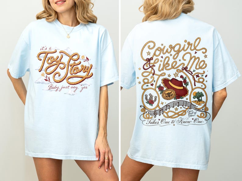 May include: A light blue t-shirt featuring a front graphic with rope-style text reading "it's a Toy Story Baby just say yes" and a back graphic with rope borders, a cowboy hat, and text reading "Cowgirl like Me Takes One to Know One".
