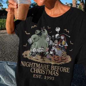 May include: Black t-shirt featuring a graphic from "The Nightmare Before Christmas" with characters like Jack Skellington, Sally, and Oogie Boogie. The text "NIGHTMARE BEFORE CHRISTMAS EST. 1993" is printed below the graphic.