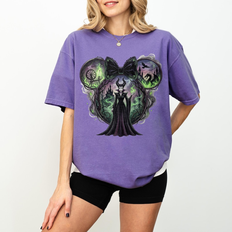 May include: A purple t-shirt featuring a graphic of a Disney villain. The design is in the shape of Mickey Mouse ears, with a black bow in the center. The graphic includes a castle, dragon, and the villain in a black dress.