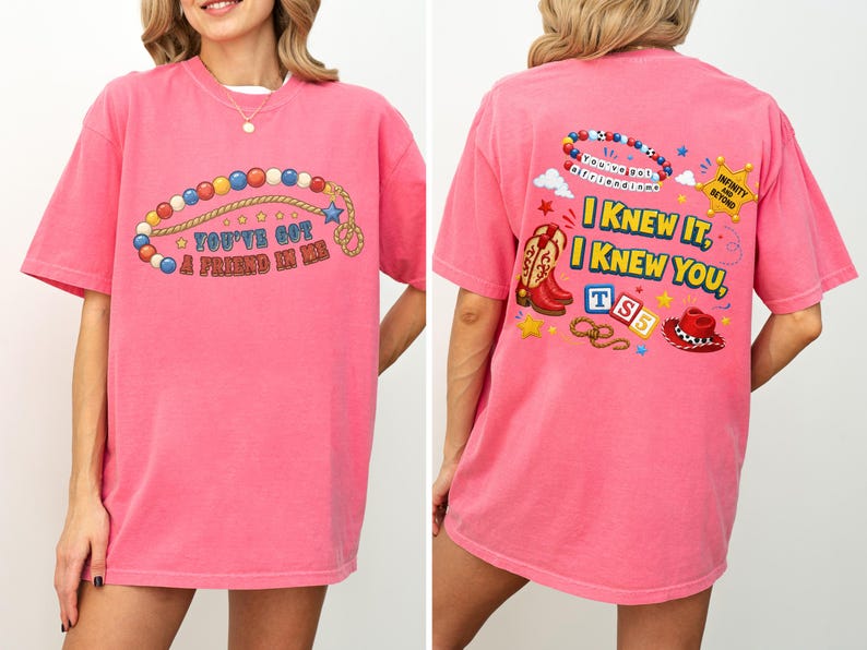 Pu&ograve; includere: Una t-shirt rosa acceso a maniche corte con una grafica frontale di una collana di perline colorate e il testo "YOU'VE GOT A FRIEND IN ME". Il retro mostra uno stivale da cowboy, una stella da sceriffo, un lazo e il testo "I KNEW IT, I KNEW YOU".