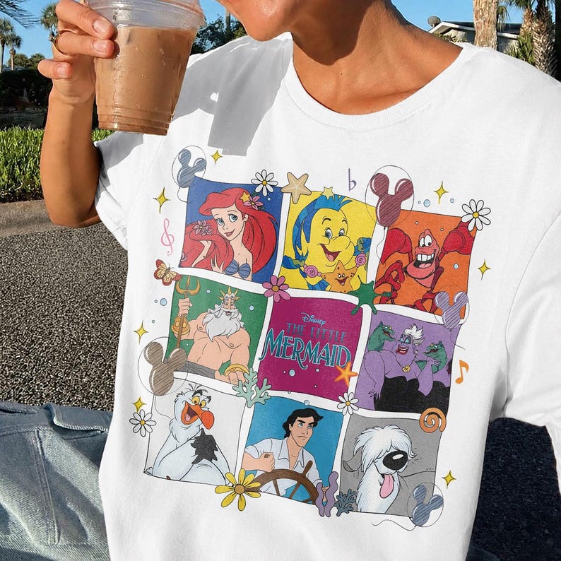 May include: White t-shirt featuring a colorful collage of characters from Disney's "The Little Mermaid." The design includes Ariel, Flounder, Sebastian, King Triton, Ursula, and Prince Eric, with the movie title in the center.