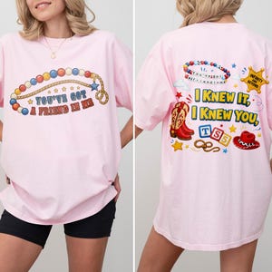 Pu&ograve; includere: Una t-shirt rosa chiaro con una grafica frontale di una collana di perline colorate e il testo "YOU'VE GOT A FRIEND IN ME". La grafica sul retro mostra una collana di perline, una stella da sceriffo con "INFINITY AND BEYOND", uno stivale, un cappello e "I KNEW IT, I KNEW YOU".