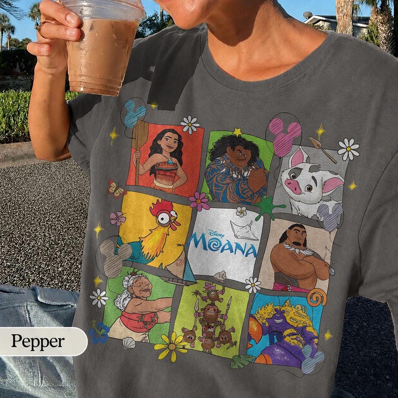 Op de afbeelding: Donkergrijs T-shirt met een kleurrijke afbeelding van personages uit de Disney-film Moana. Het ontwerp bevat afbeeldingen van Moana, Maui, Pua, Hei Hei en anderen, met het Disney Moana-logo. Een casual kledingstuk.