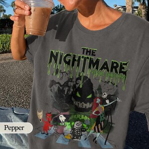 K&ouml;nnte beinhalten: Graues T-Shirt mit dem Text "THE NIGHTMARE BEFORE CHRISTMAS" in tropfenden gr&uuml;nen Buchstaben. Die Grafik zeigt Charaktere aus dem Film. Das T-Shirt hat einen Rundhalsausschnitt.