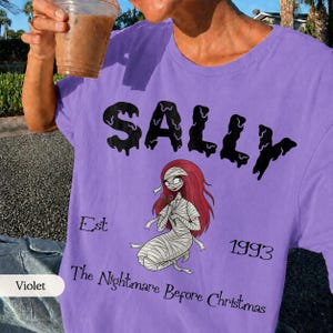 May include: Violet-colored t-shirt featuring the name "SALLY" in black dripping font, with an illustration of Sally from "The Nightmare Before Christmas." The shirt also includes the text "Est 1993" and "The Nightmare Before Christmas."
