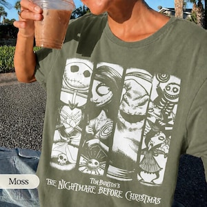 K&ouml;nnte beinhalten: Ein moosgr&uuml;nes T-Shirt mit einem wei&szlig;en Grafikdruck von Charakteren aus Tim Burton's The Nightmare Before Christmas. Das Design besteht aus vier vertikalen Feldern, die Jack Skellington, Sally, Oogie Boogie und weitere Figuren zeigen.