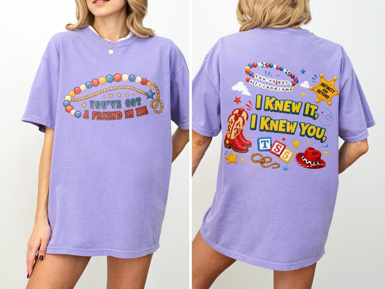 Pu&ograve; includere: Una t-shirt viola chiaro con una grafica sul davanti e sul retro. Il davanti mostra una collana di perline e il testo "You've got a friend in me". Il retro mostra perline, una stella da sceriffo, stivali da cowboy, blocchi e un cappello.