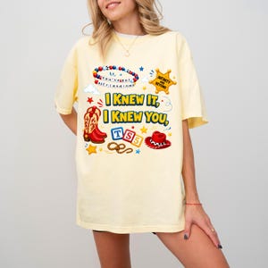 May include: A pale yellow t-shirt featuring a graphic print with the text "I KNEW IT, I KNEW YOU," a beaded bracelet with "You've got a friend in me," a sheriff star with "INFINITY AND BEYOND," cowboy boots, a lasso, and a red cowboy hat.