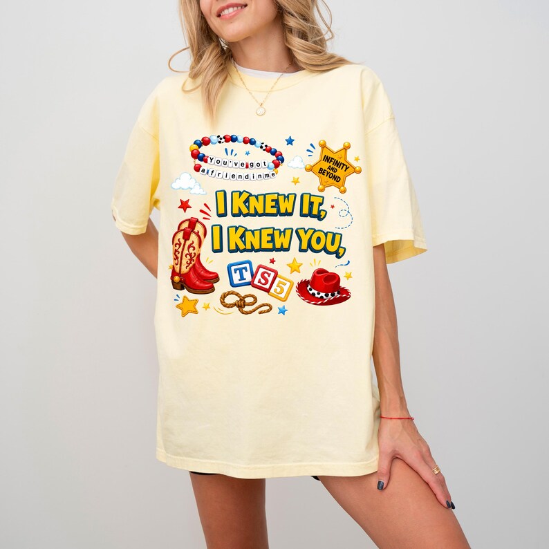 May include: A pale yellow t-shirt featuring a graphic print with the text "I KNEW IT, I KNEW YOU," a beaded bracelet with "You've got a friend in me," a sheriff star with "INFINITY AND BEYOND," cowboy boots, a lasso, and a red cowboy hat.