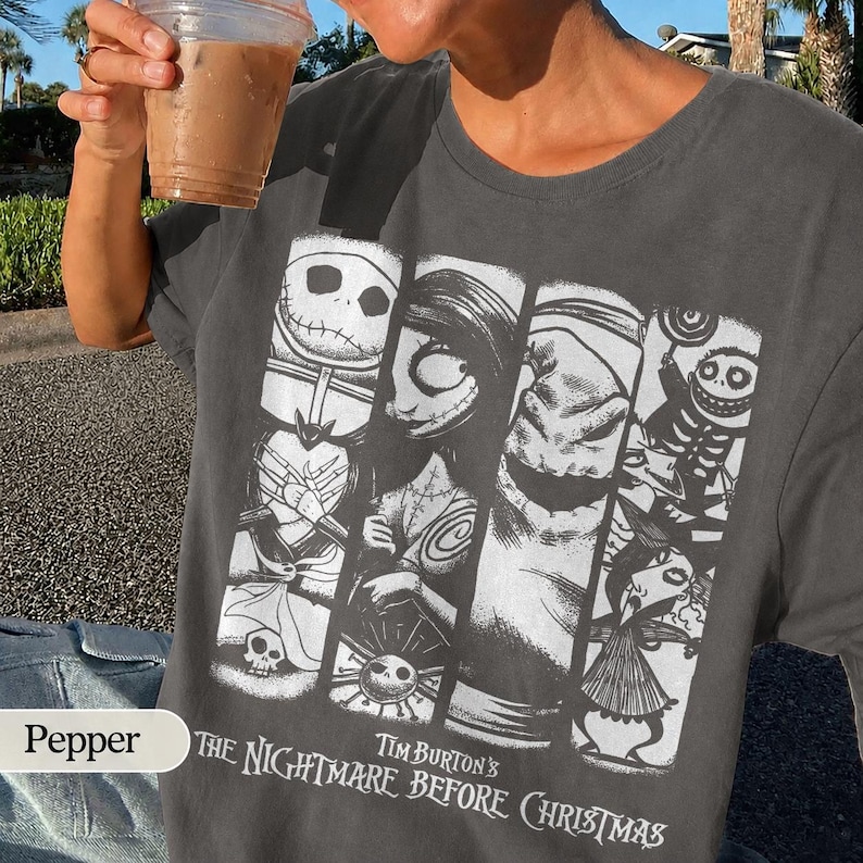 K&ouml;nnte beinhalten: Ein anthrazitfarbenes T-Shirt mit einem wei&szlig;en Grafikdruck von Charakteren aus Tim Burtons Nightmare Before Christmas, darunter Jack Skellington, Sally und Oogie Boogie, angeordnet in vertikalen Feldern mit dem Filmtiteltext darunter.