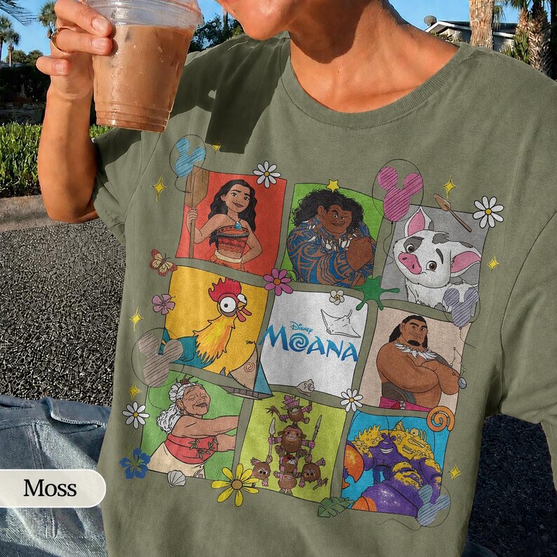 Op de afbeelding: Mosgroen t-shirt met een kleurrijke afbeelding van personages uit de Disney-film Moana. Het ontwerp bevat Moana, Maui, Pua, Hei Hei en andere personages. Het shirt heeft een ronde hals en korte mouwen.