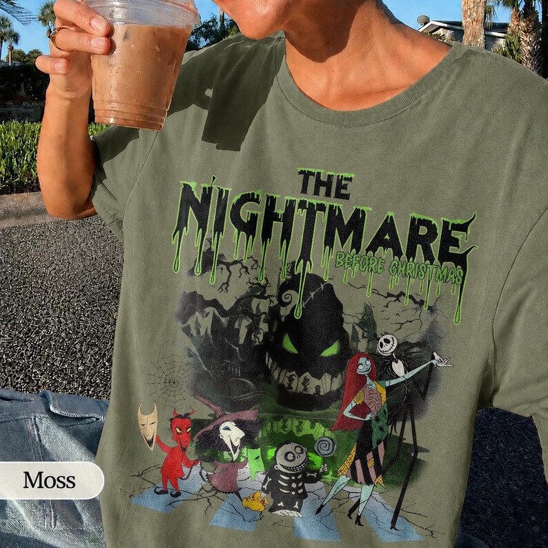 K&ouml;nnte beinhalten: Moosgr&uuml;nes T-Shirt mit einem Grafikmotiv aus "The Nightmare Before Christmas". Das Design zeigt den Filmtitel in tropfenden gr&uuml;nen Buchstaben, mit Figuren wie Jack Skellington und Sally. Das Shirt hat eine lockere Passform.