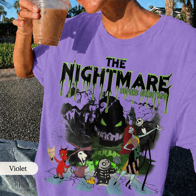 K&ouml;nnte beinhalten: Ein violettes T-Shirt mit einer Grafik aus "The Nightmare Before Christmas". Das Design zeigt Charaktere wie Jack Skellington, Sally und Oogie Boogie, mit dem Filmtitel in Gr&uuml;n und Schwarz.