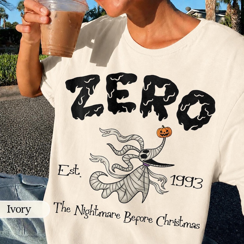 May include: Ivory-colored t-shirt featuring the word "ZERO" in a dripping black font. Below, a cartoon ghost with a pumpkin head and the text "Est. 1993 The Nightmare Before Christmas".
