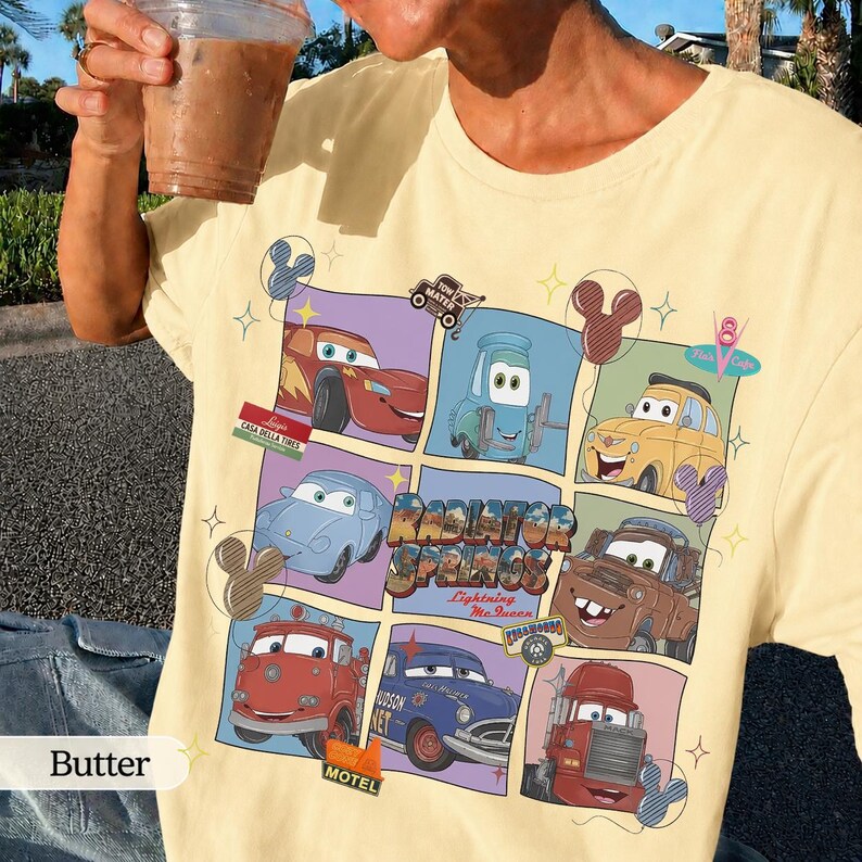 May include: A pale yellow t-shirt featuring a grid graphic of characters from the movie Cars, including Lightning McQueen, Mater, and others. The design includes the text Radiator Springs and Lightning McQueen, accented with small Mickey Mouse icons.