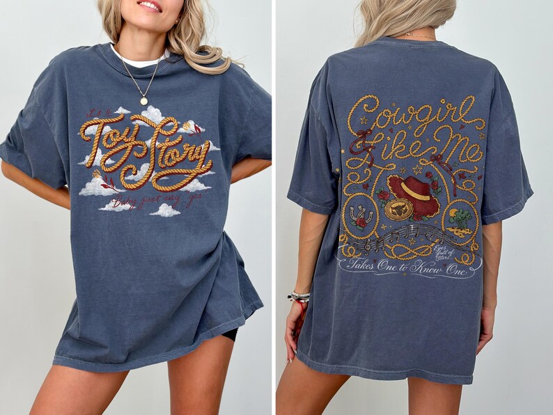 May include: A slate blue t-shirt featuring a front graphic with the text Toy Story in rope-style lettering over white clouds. The back graphic displays the text Cowgirl Like Me with a cowboy hat, rope accents, and the text Takes One to Know One.