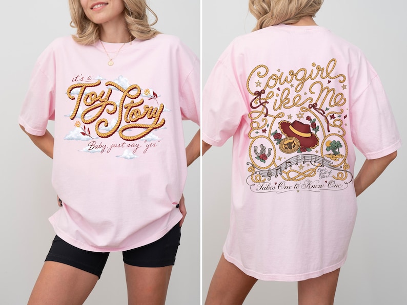 May include: A light pink t-shirt featuring a graphic on the front that reads "it's a Toy Story Baby just say yes" in rope-style lettering. The back graphic displays "Cowgirl like Me" and "Takes One to Know One" with a cowboy hat and rope motifs.