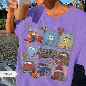 May include: A violet t-shirt featuring a grid of characters from the movie Cars, including Lightning McQueen, Mater, and Sally. The center text reads Radiator Springs Lightning McQueen, surrounded by small icons of Mickey Mouse ears and stars.
