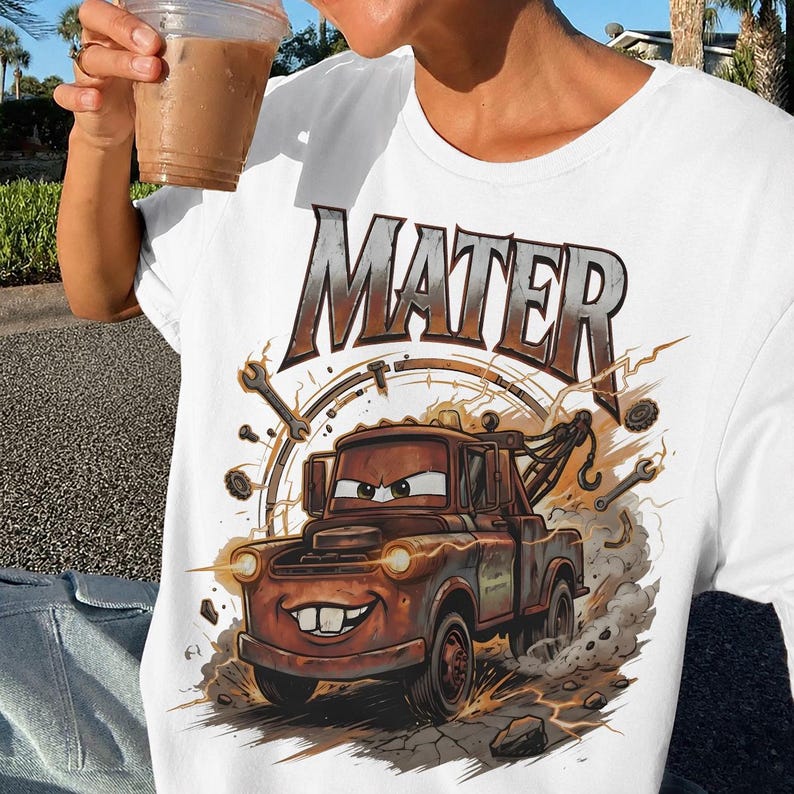 May include: White t-shirt featuring a cartoon image of Mater from the movie Cars. The image shows Mater, a brown tow truck, with the word "MATER" above him. The design includes wrenches and a circular background.