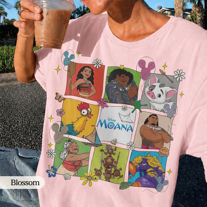 Op de afbeelding: Zachtroze T-shirt met een kleurrijke afbeelding van personages uit de Disney-film Moana. Het ontwerp bevat Moana, Maui, Pua, Hei Hei en anderen. Het shirt heeft een ronde hals en korte mouwen.