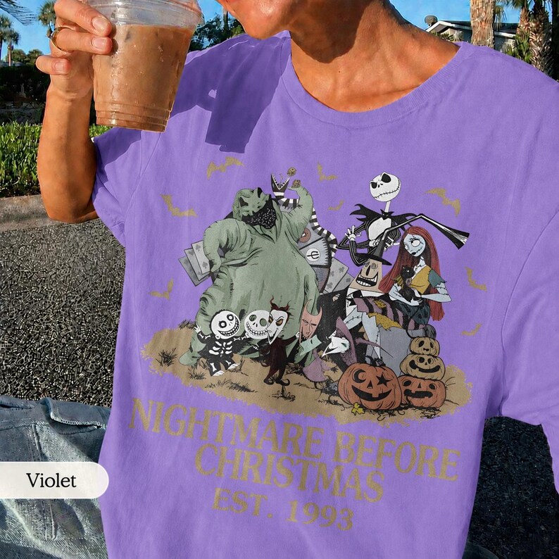 May include: Violet-colored t-shirt featuring a graphic from "The Nightmare Before Christmas." The design includes characters like Jack Skellington, Sally, and Oogie Boogie, along with pumpkins and the text "NIGHTMARE BEFORE CHRISTMAS EST. 1993."
