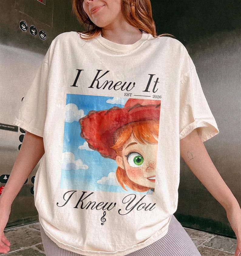 K&ouml;nnte beinhalten: Ein cremefarbenes Kurzarm-T-Shirt mit einem Grafikdruck einer Zeichentrickfigur mit roten Haaren und einem roten Hut vor einem blauen Himmel mit Wolken. Der Text "I Knew It" steht &uuml;ber der Grafik und "I Knew You" ist darunter gedruckt.