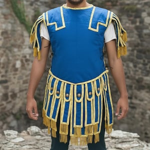 Peut inclure: Un costume bleu et or de style romain avec un sous-vêtement blanc. Le costume présente des bordures et des franges dorées, avec une jupe et des épaulettes assorties. La personne porte un pantalon bleu foncé.