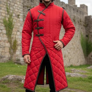 May include: A red quilted coat with a diamond pattern, featuring brown trim and leather straps. The long coat has a high collar and is worn over black pants. The background shows a stone castle.
