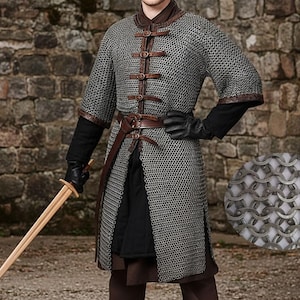 May include: A medieval-style chainmail shirt with leather accents and a brown leather belt. The shirt has short sleeves and is fastened with leather straps. A wooden sword is held in the left hand. The background is a stone wall.