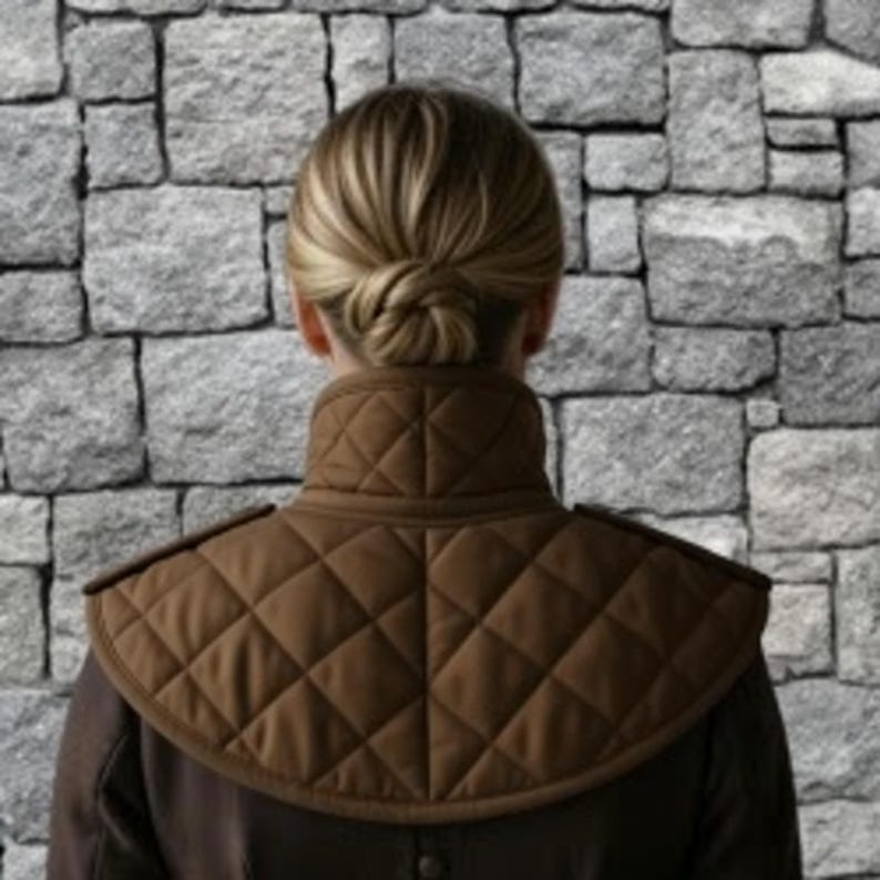 May include: A brown quilted shoulder cape with a high collar. The cape has a diamond pattern and is worn over a dark-colored garment. The background is a stone wall.