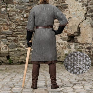 May include: A person wearing a chainmail shirt, brown pants, and boots, holding a wooden sword. The chainmail is silver and worn over a brown tunic. The person is wearing black gloves and a brown belt.