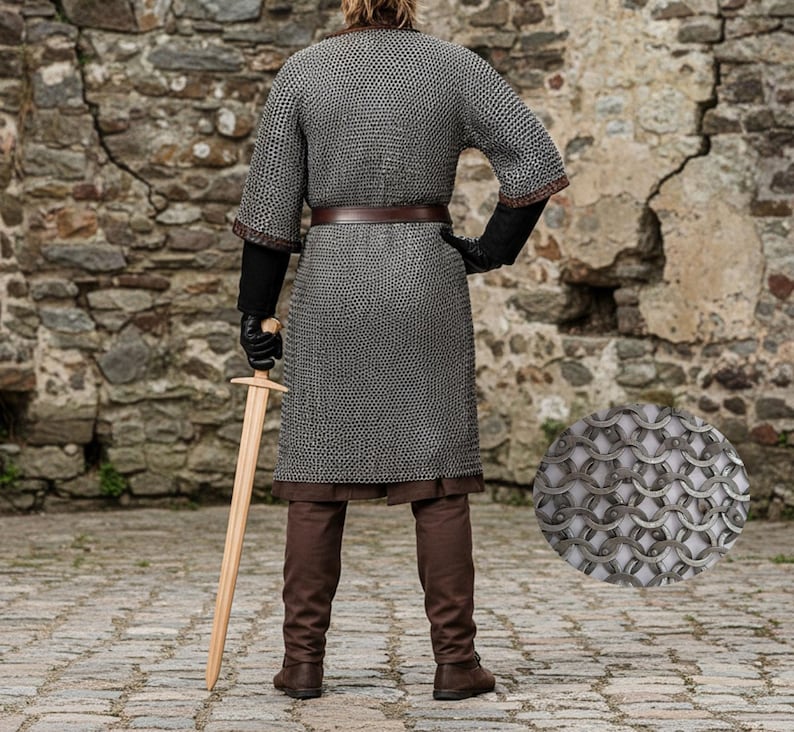 May include: A person wearing a chainmail shirt, brown pants, and boots, holding a wooden sword. The chainmail is silver and worn over a brown tunic. The person is wearing black gloves and a brown belt.