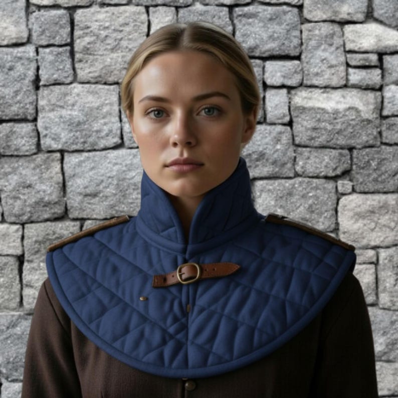May include: A quilted navy blue neck guard with brown leather accents and a buckle closure. The neck guard has a diamond pattern and is worn over a brown garment. The background is a stone wall.